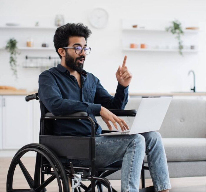 man in wheelchair pointing in front of laptop
